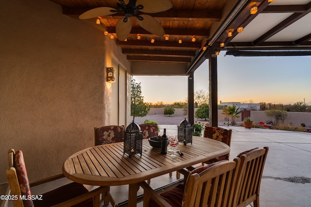 patio terrace at dusk with ceiling fan, outdoor dining space, and fence