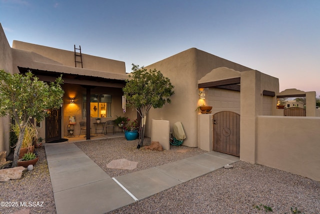 pueblo-style house with a gate, fence, a garage, and stucco siding