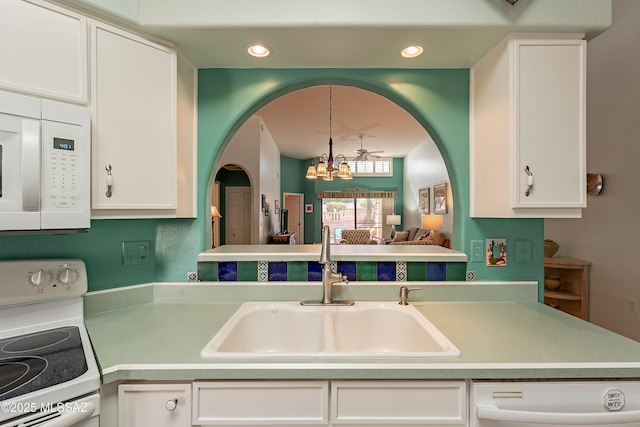 kitchen with white appliances, arched walkways, a chandelier, white cabinetry, and a sink