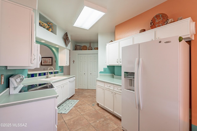 kitchen featuring white appliances, light countertops, a sink, and white cabinetry