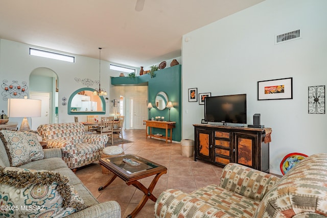 living area featuring a high ceiling, visible vents, arched walkways, and tile patterned floors