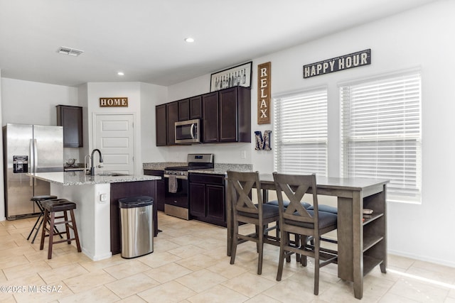 kitchen featuring dark brown cabinetry, visible vents, light stone counters, stainless steel appliances, and a sink