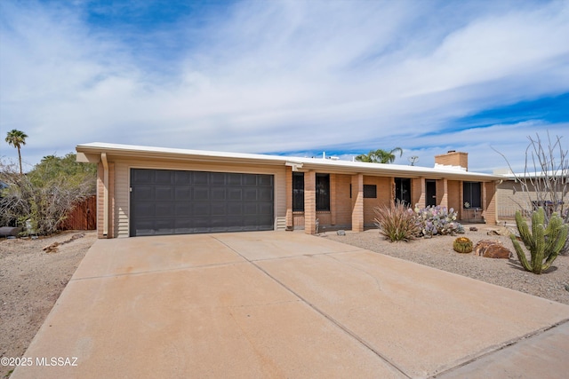 ranch-style house featuring driveway, brick siding, a chimney, and an attached garage