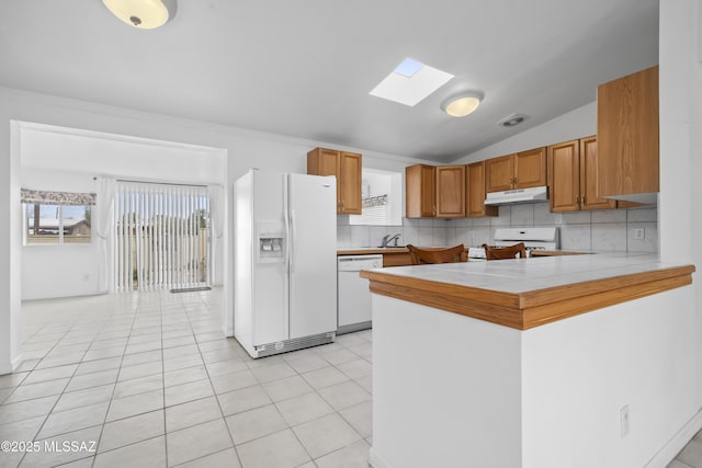 kitchen with white appliances, under cabinet range hood, decorative backsplash, and tile countertops