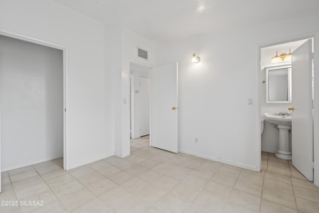 unfurnished bedroom with ensuite bath, baseboards, light tile patterned floors, and visible vents