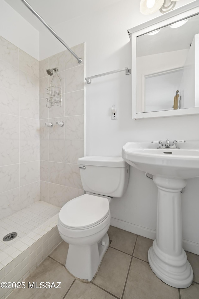 full bath with toilet, baseboards, a tile shower, and tile patterned floors