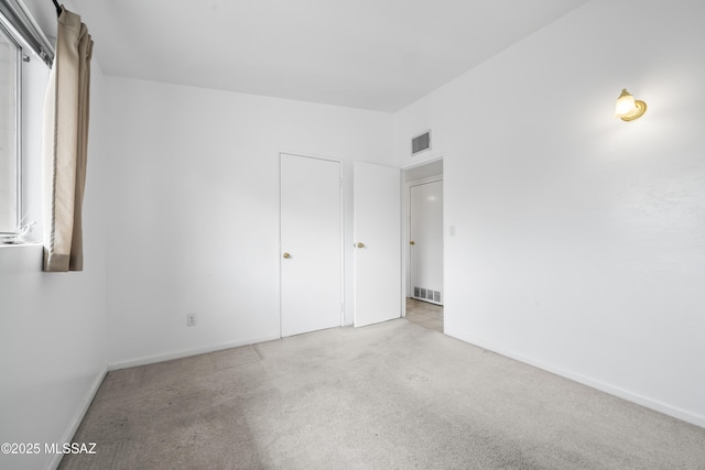 unfurnished bedroom with carpet, visible vents, vaulted ceiling, and baseboards