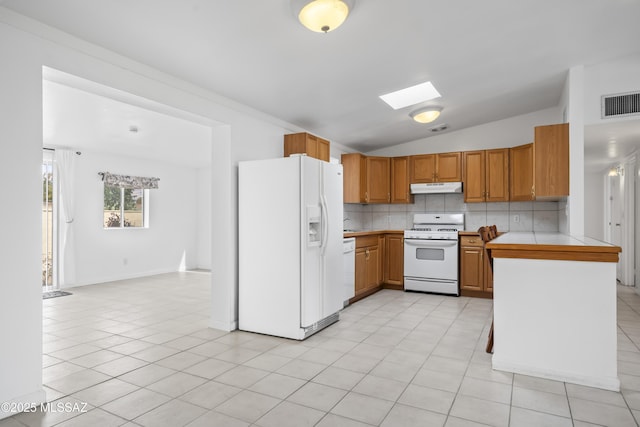 kitchen with white appliances, vaulted ceiling with skylight, tasteful backsplash, visible vents, and under cabinet range hood