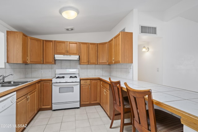 kitchen featuring white appliances, tasteful backsplash, visible vents, under cabinet range hood, and a sink