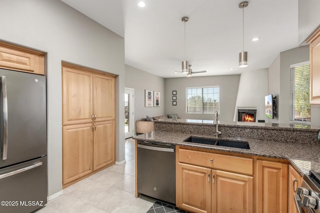 kitchen with appliances with stainless steel finishes, open floor plan, a sink, and dark stone counters