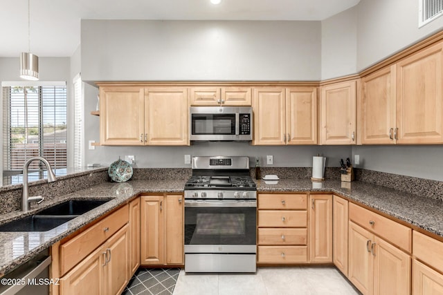 kitchen featuring dark stone countertops, stainless steel appliances, a sink, and light brown cabinetry