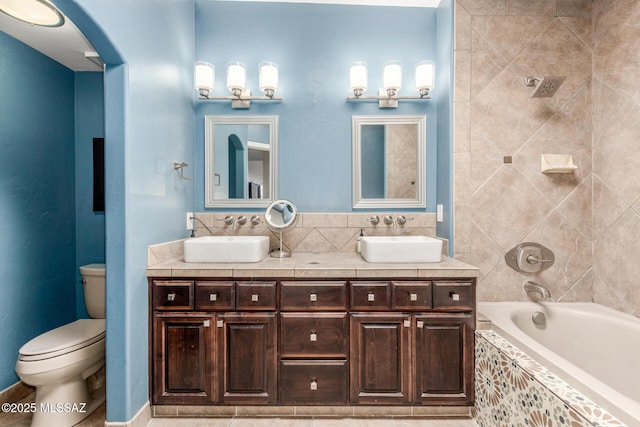 bathroom with a sink, tiled shower / bath, toilet, and double vanity