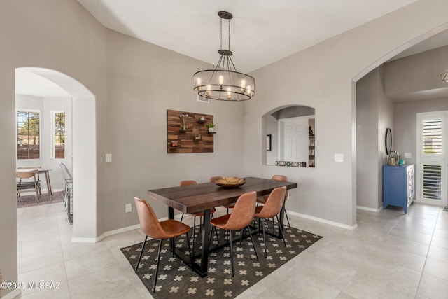 dining room with an inviting chandelier, baseboards, arched walkways, and light tile patterned flooring