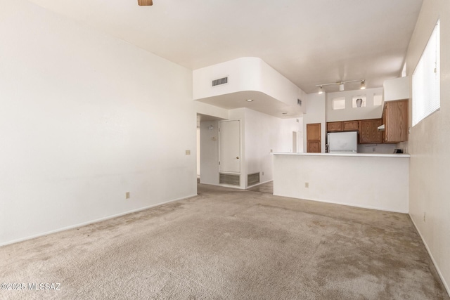 unfurnished living room featuring visible vents, track lighting, and light colored carpet