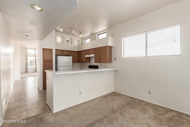 kitchen featuring plenty of natural light, freestanding refrigerator, a peninsula, light countertops, and under cabinet range hood