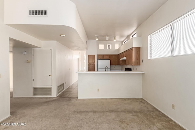 kitchen featuring light colored carpet, freestanding refrigerator, visible vents, and a peninsula