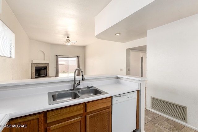 kitchen featuring white dishwasher, a sink, visible vents, light countertops, and brown cabinetry