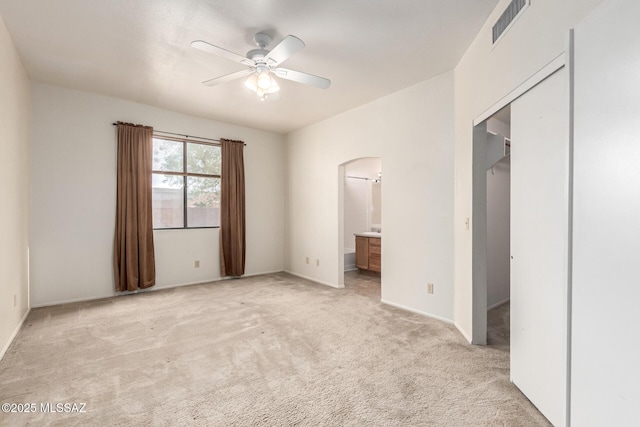 unfurnished bedroom with visible vents, arched walkways, light colored carpet, ceiling fan, and ensuite bathroom