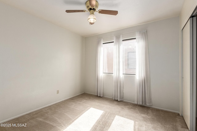 spare room with a ceiling fan, light carpet, and baseboards