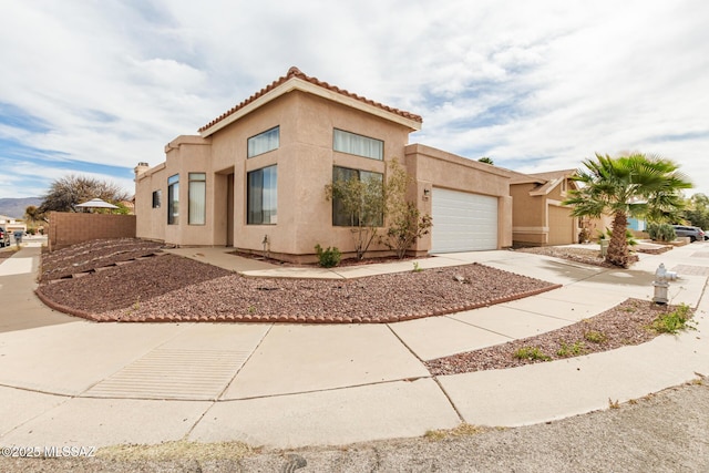 mediterranean / spanish house featuring an attached garage, fence, driveway, a tiled roof, and stucco siding