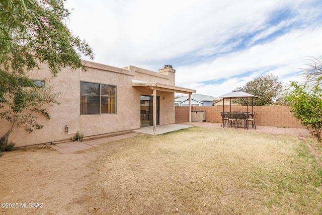 rear view of property with a chimney, stucco siding, a lawn, a patio area, and fence