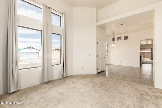 carpeted empty room featuring an inviting chandelier, tile patterned flooring, and a high ceiling