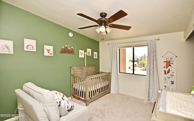 carpeted bedroom featuring a nursery area, a ceiling fan, and baseboards