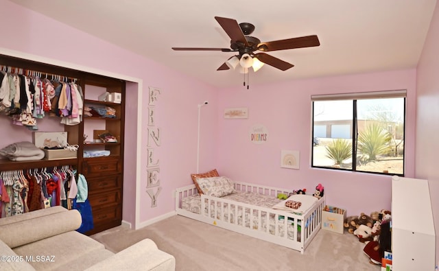 carpeted bedroom with a crib, baseboards, and a ceiling fan