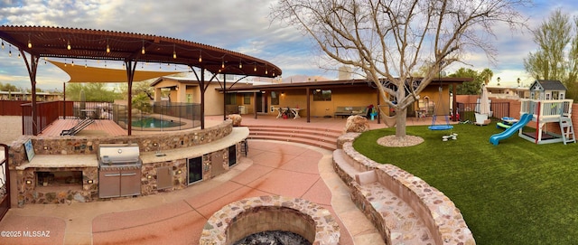 view of patio / terrace with playground community, area for grilling, fence, exterior kitchen, and a fire pit