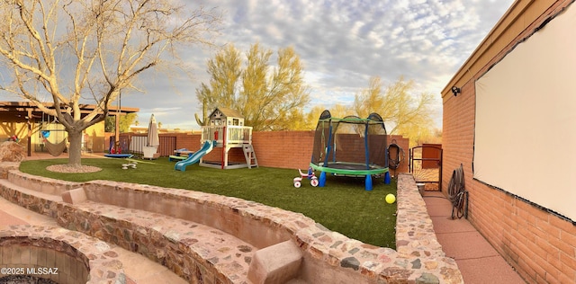 community playground featuring a trampoline, a fenced backyard, and a lawn