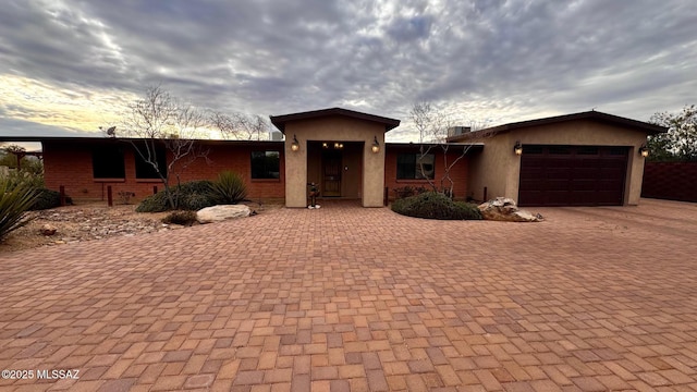 view of front of home featuring a garage, decorative driveway, brick siding, and stucco siding