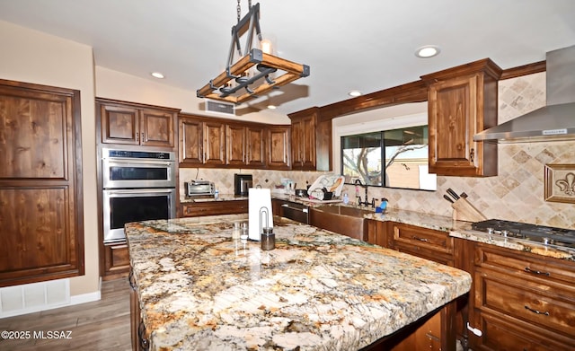 kitchen with light stone counters, stainless steel double oven, a sink, visible vents, and wall chimney exhaust hood