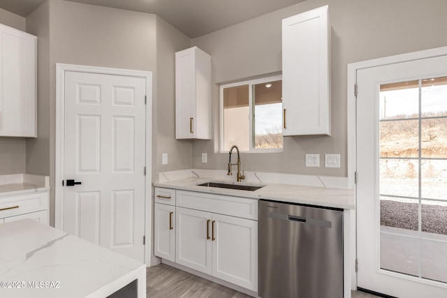 kitchen with light stone counters, white cabinets, dishwasher, and a sink