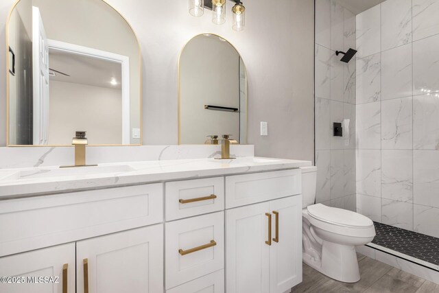 full bathroom featuring a tile shower, double vanity, a sink, and toilet