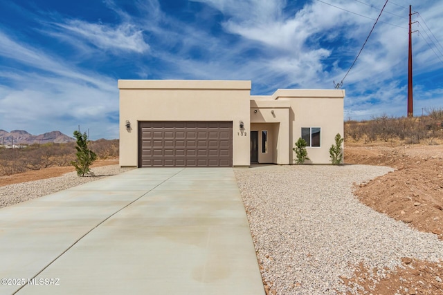 pueblo-style home featuring concrete driveway, an attached garage, a mountain view, and stucco siding