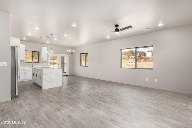 unfurnished living room featuring recessed lighting, visible vents, light wood finished floors, and ceiling fan with notable chandelier