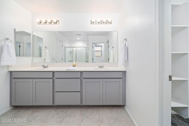 bathroom with a stall shower, a sink, baseboards, and double vanity