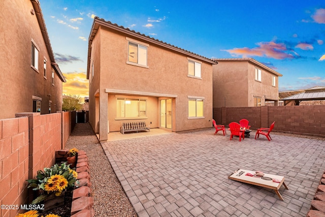 back of property at dusk featuring a patio area, a fenced backyard, and stucco siding