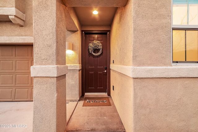 entrance to property with a garage and stucco siding