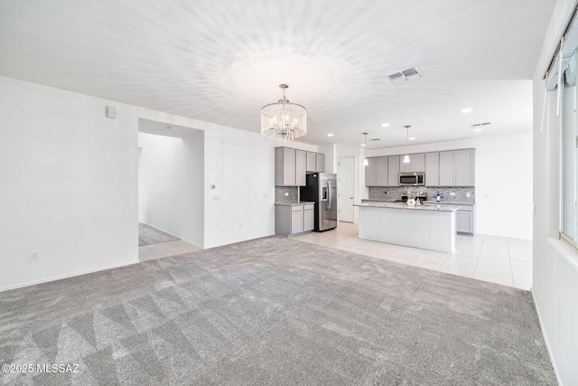 unfurnished living room featuring light tile patterned floors, light colored carpet, visible vents, and an inviting chandelier