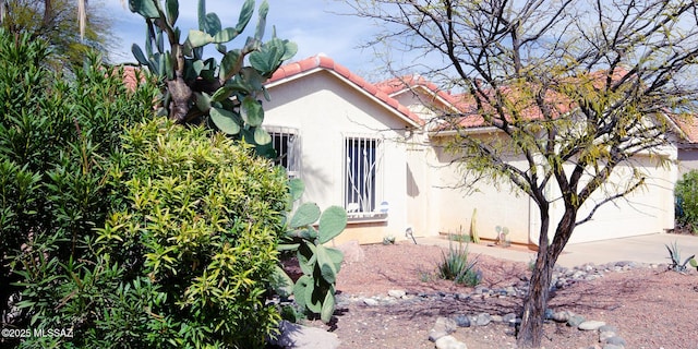 view of home's exterior with a garage, concrete driveway, a tile roof, and stucco siding