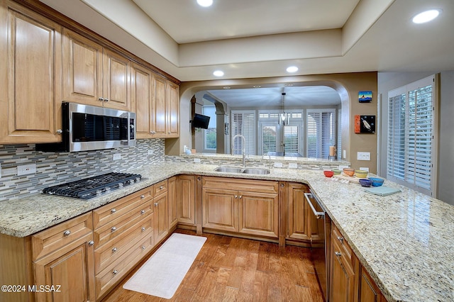 kitchen with light wood finished floors, tasteful backsplash, light stone counters, appliances with stainless steel finishes, and a sink