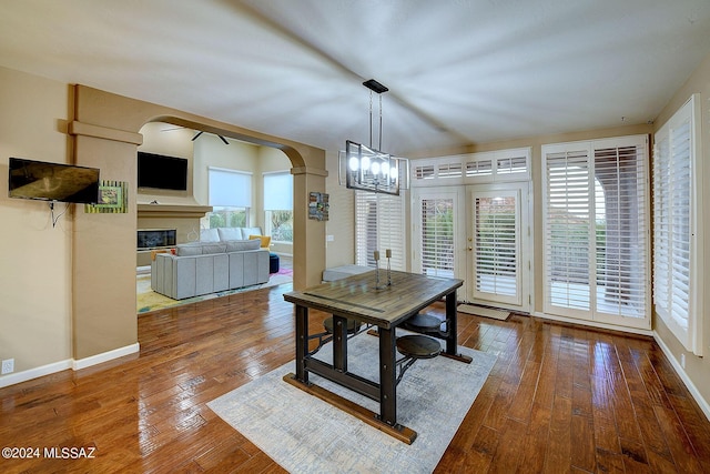 dining room featuring hardwood / wood-style floors, a glass covered fireplace, arched walkways, an inviting chandelier, and baseboards