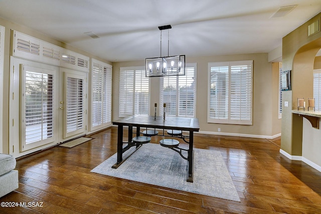 dining area with hardwood / wood-style flooring, a notable chandelier, arched walkways, and baseboards