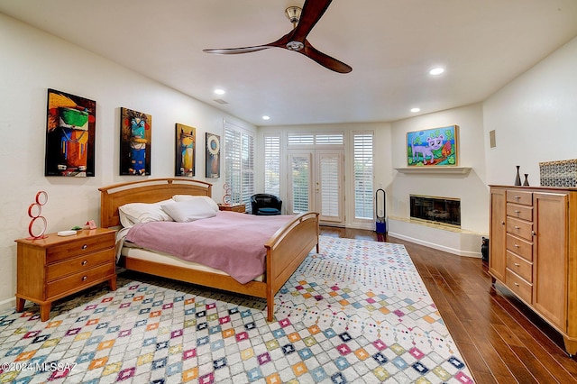 bedroom featuring ceiling fan, a glass covered fireplace, wood finished floors, recessed lighting, and access to exterior