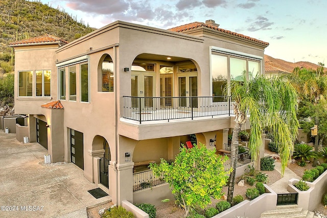 rear view of property featuring a balcony, french doors, driveway, and stucco siding