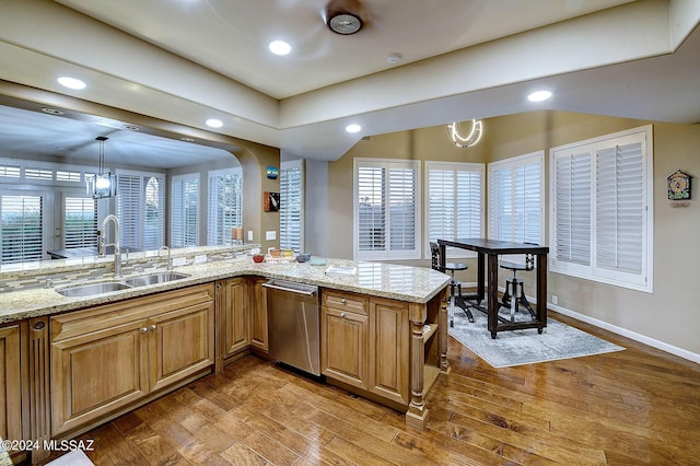 kitchen featuring light stone counters, dishwasher, wood finished floors, and a sink