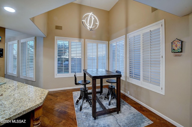 dining space featuring dark wood-style floors, visible vents, baseboards, high vaulted ceiling, and an inviting chandelier