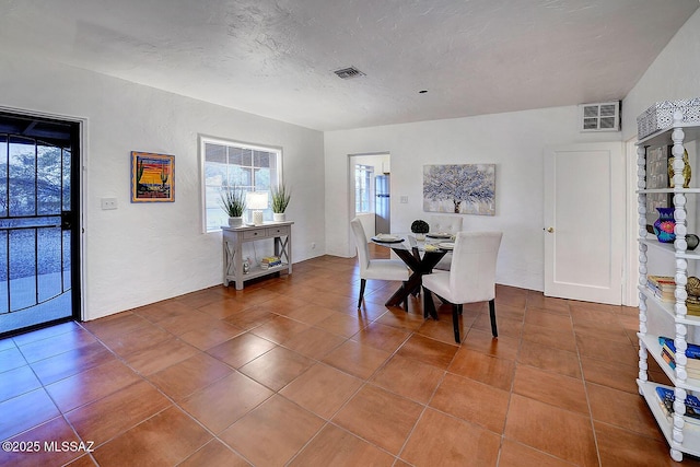 tiled dining area with visible vents, a textured ceiling, and a textured wall