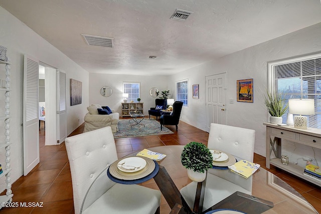 tiled dining area featuring visible vents, a textured ceiling, and a textured wall